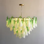 The Clérachic chandelier in sage green glass petals on a brass chain, full silhouette lit from below.