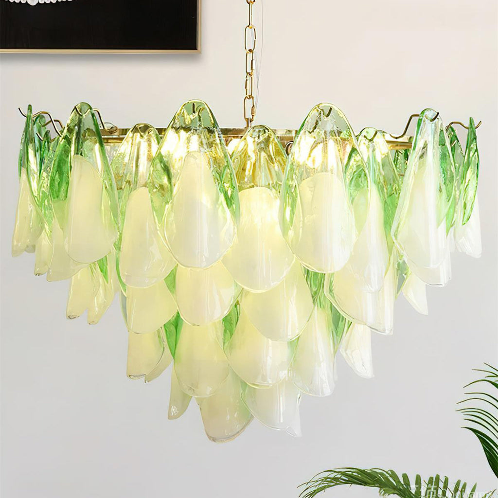 Clérachic chandelier in sage green glass petals lit in a living room corner with a leafy plant.