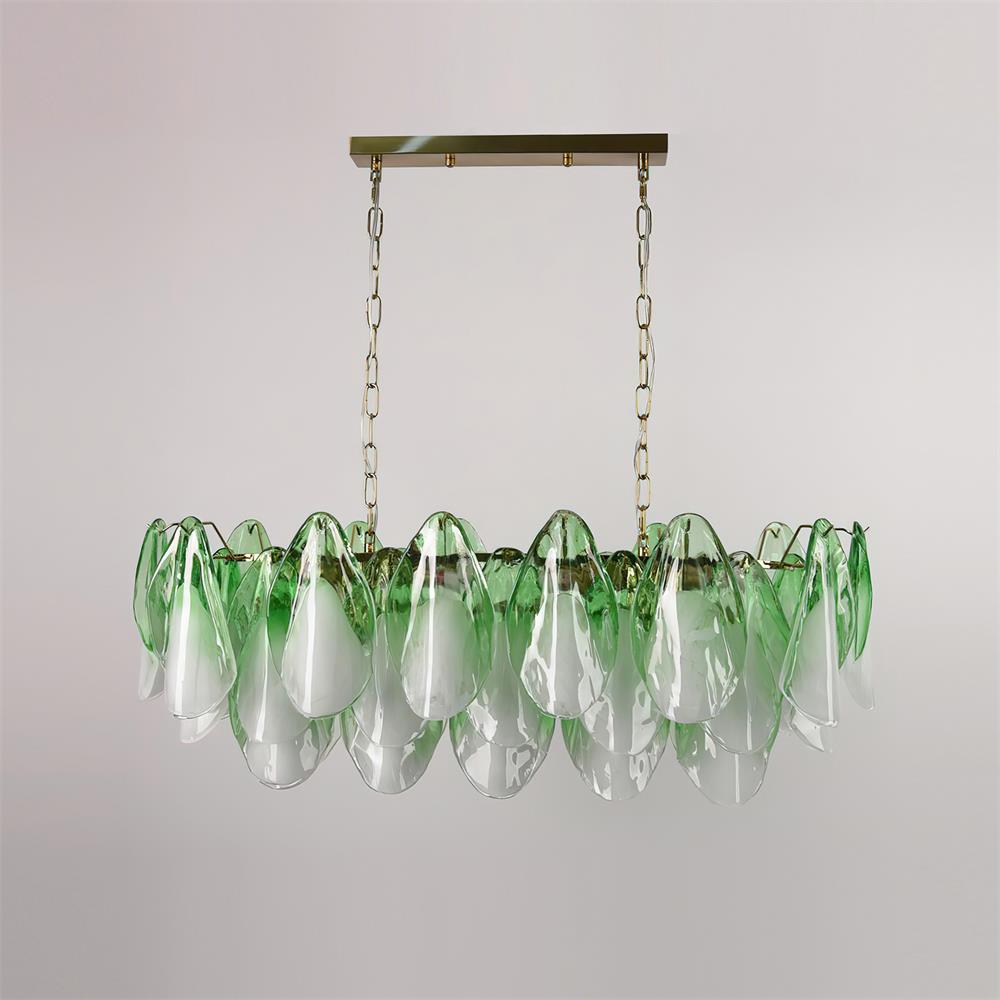The Clérachic linear chandelier in sage green glass petals hangs on a brass chain over a long table.