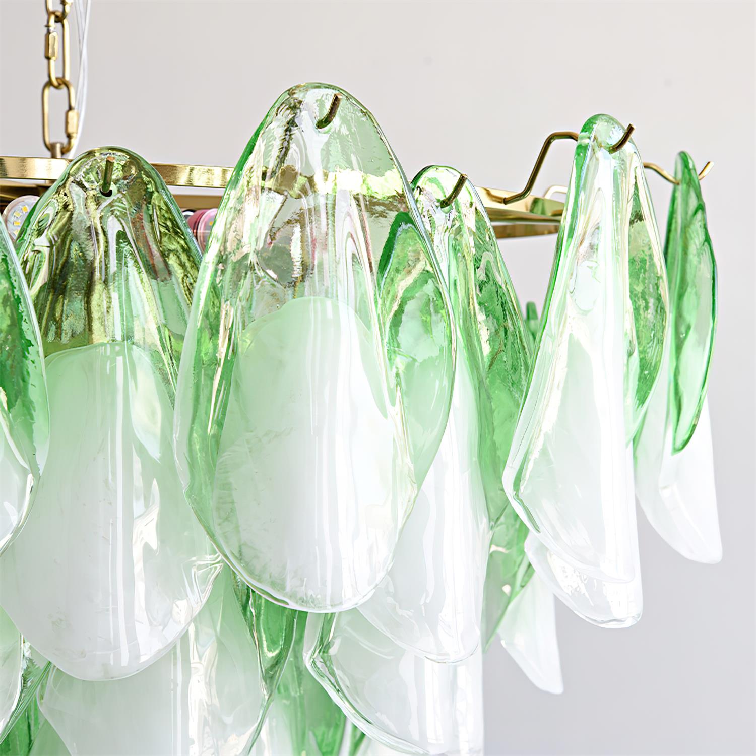 Clérachic close-up of sage green glass petals cascading from the brass frame, edges catching light.