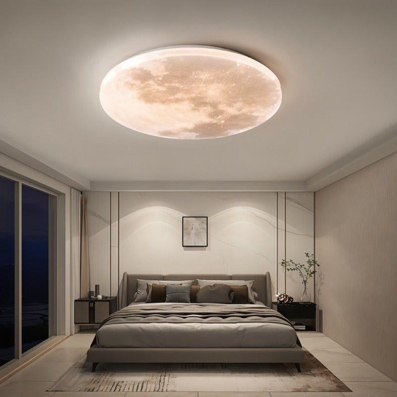 Clérachic moon-disc ceiling light glowing warm above a grey upholstered bed in a calm, marble-panelled bedroom at night.