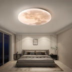 Clérachic moon-disc ceiling light glowing warm above a grey upholstered bed in a calm, marble-panelled bedroom at night.