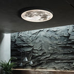 Clérachic black-rimmed moon ceiling light glowing against a dark ceiling, with a textured slate wall and pendant lights below.
