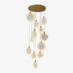A Clérachic pendant cluster of round alabaster discs at different heights on slim cords, hanging from a gold ceiling plate, on a white backdrop.