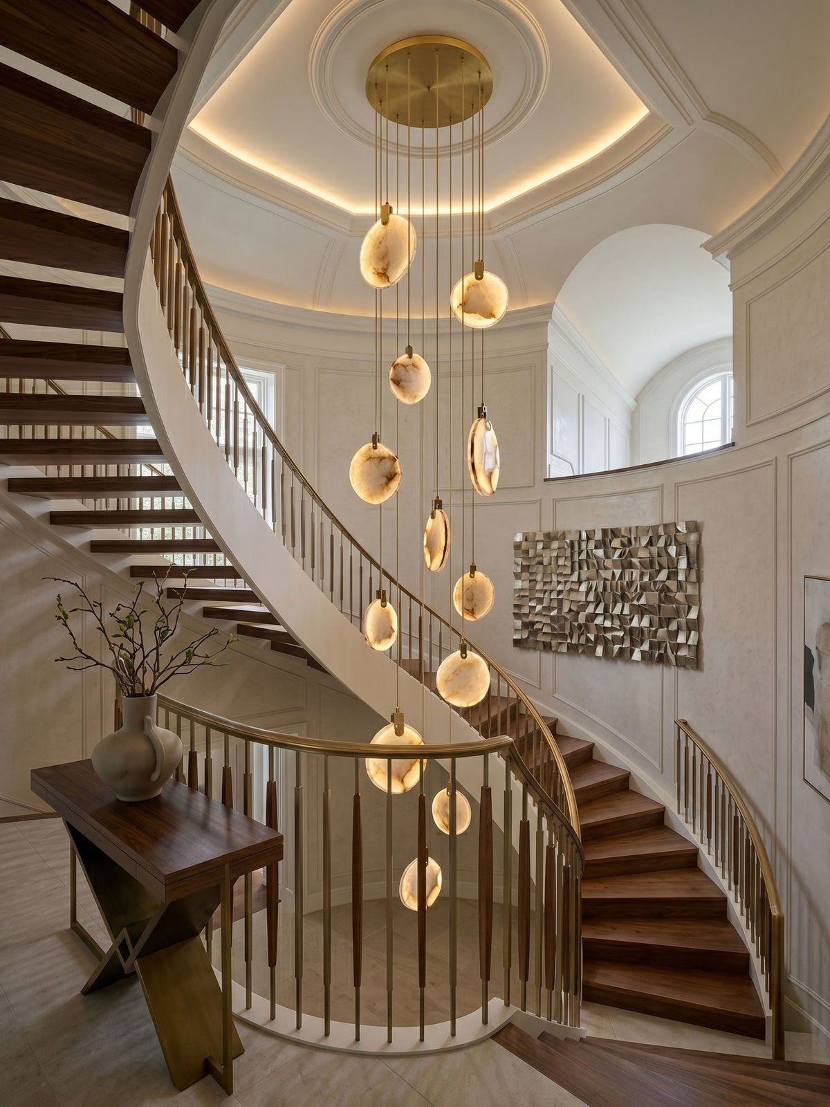 A Clérachic cluster of lit alabaster discs hangs from a round gold canopy in a domed stairwell with a curved timber staircase.