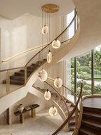 Lit alabaster disc pendants from Clérachic fall past a sweeping cream staircase with timber treads and a garden view.