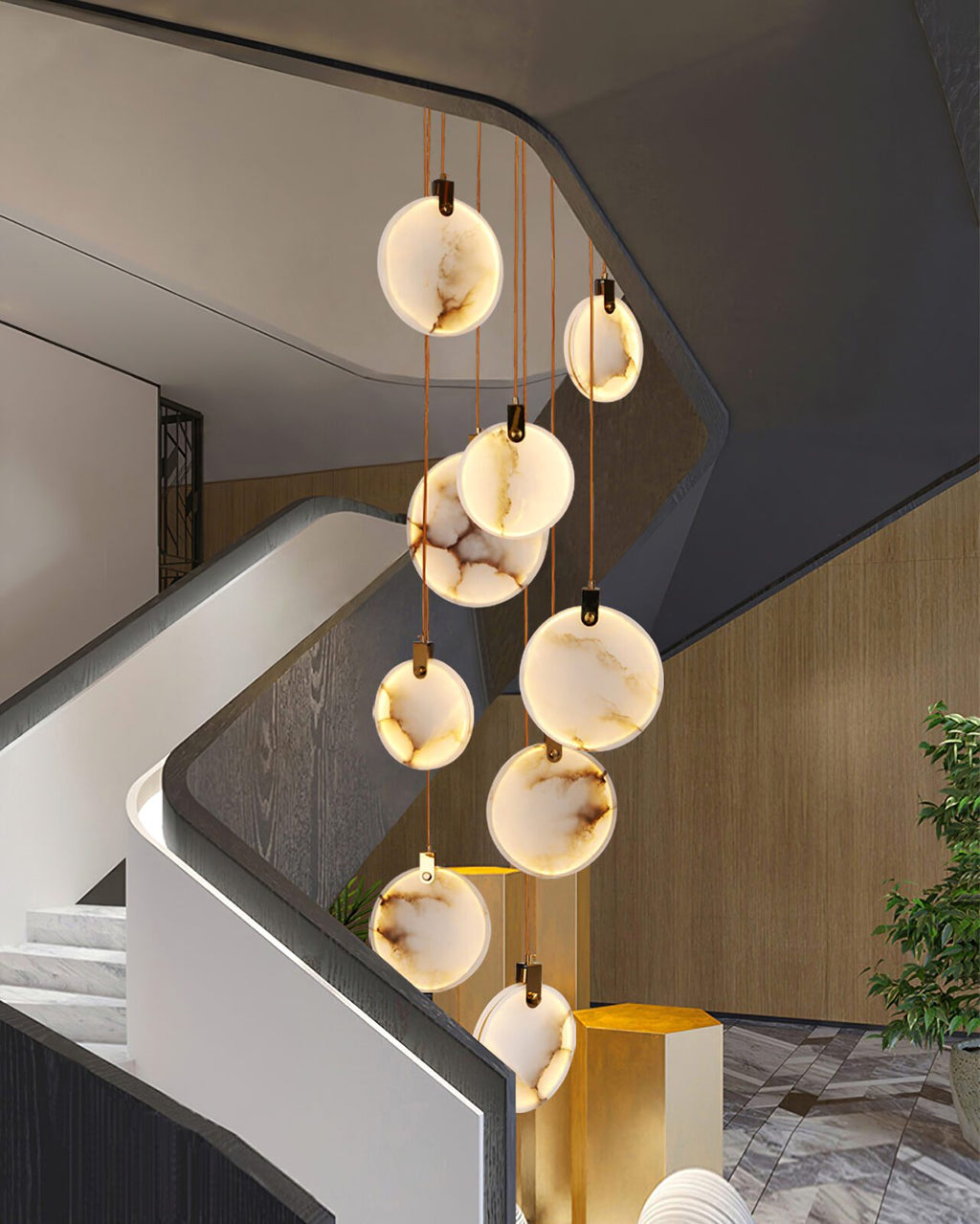 A Clérachic alabaster disc cluster hangs beside a curving white stair and a timber wall, with a plant and a gold stool below.