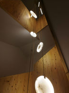 Clérachic alabaster discs glow in a stairwell lined with pale knotty timber, with a bright disc in the lower right.