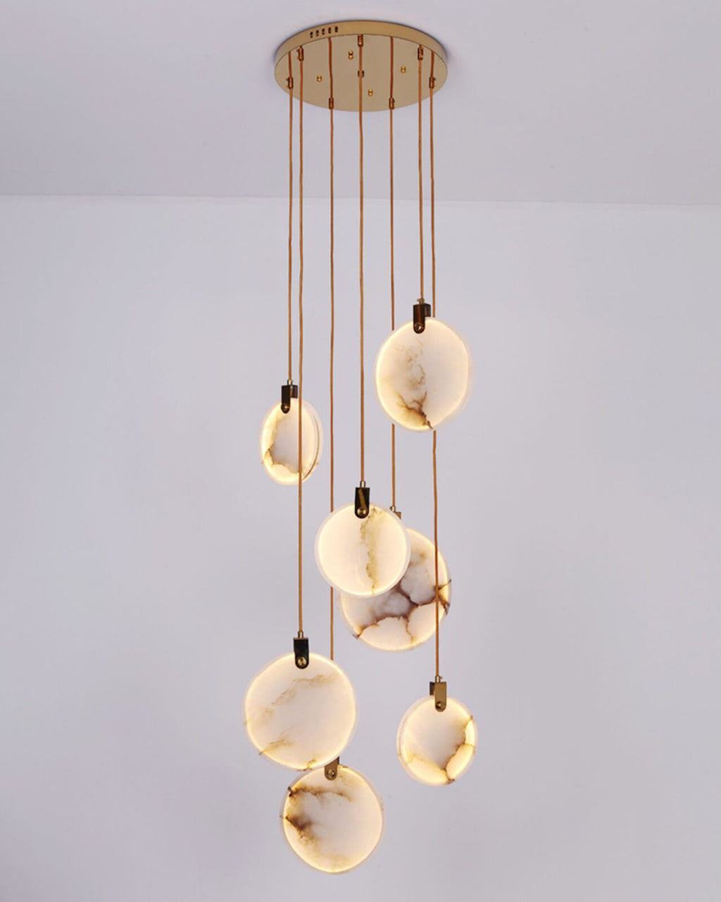 A Clérachic alabaster disc cluster of lit, veined discs on tan cords from a round gold canopy, on a pale lilac backdrop.