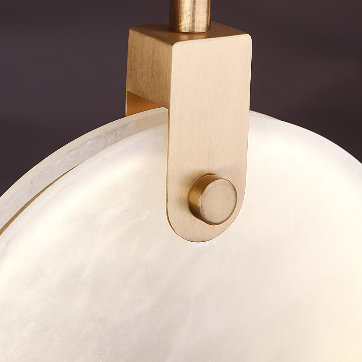 Close view of the brushed gold bracket and fixing screw that holds one alabaster disc on this Clérachic pendant.