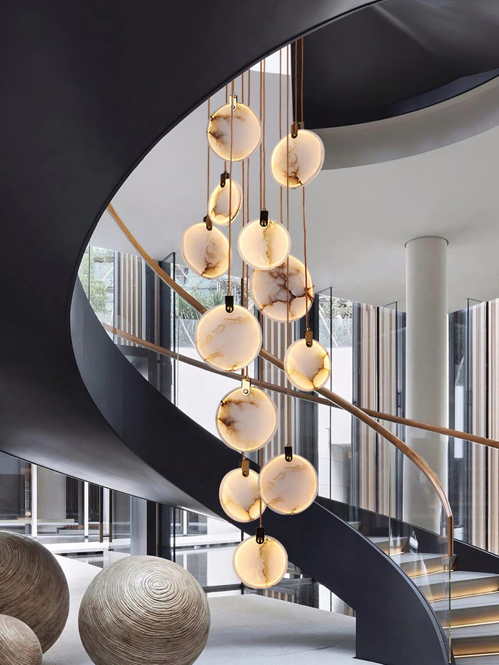 Clérachic alabaster discs hang in front of a black spiral stair with glass walls and two round woven sculptures at its foot.
