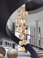Clérachic alabaster discs hang in front of a black spiral stair with glass walls and two round woven sculptures at its foot.
