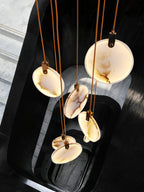 Looking straight down on veined alabaster discs on tan cords from this Clérachic pendant, over a black stairwell.