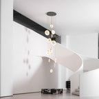 A Clérachic alabaster disc cluster on a dark ceiling plate hangs beside a white sculptural staircase with a black marble block below.