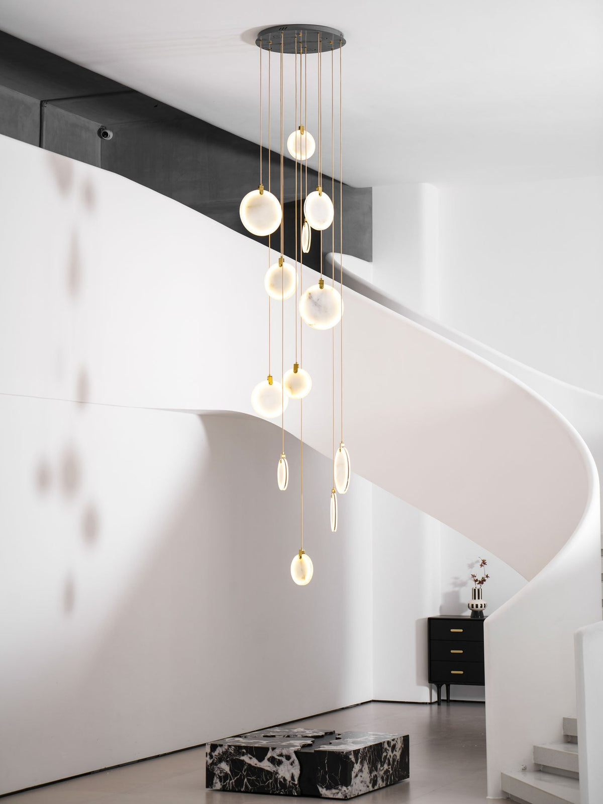 A closer view of the lit Clérachic disc cluster beside a curving white staircase, with a black sideboard in the distance.