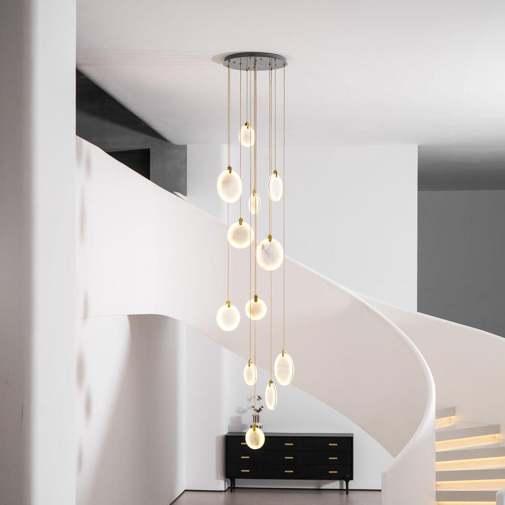 Lit Clérachic alabaster discs fall in a column in front of a white curving staircase with softly lit steps and a black sideboard.