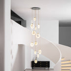 Lit Clérachic alabaster discs fall in a column in front of a white curving staircase with softly lit steps and a black sideboard.
