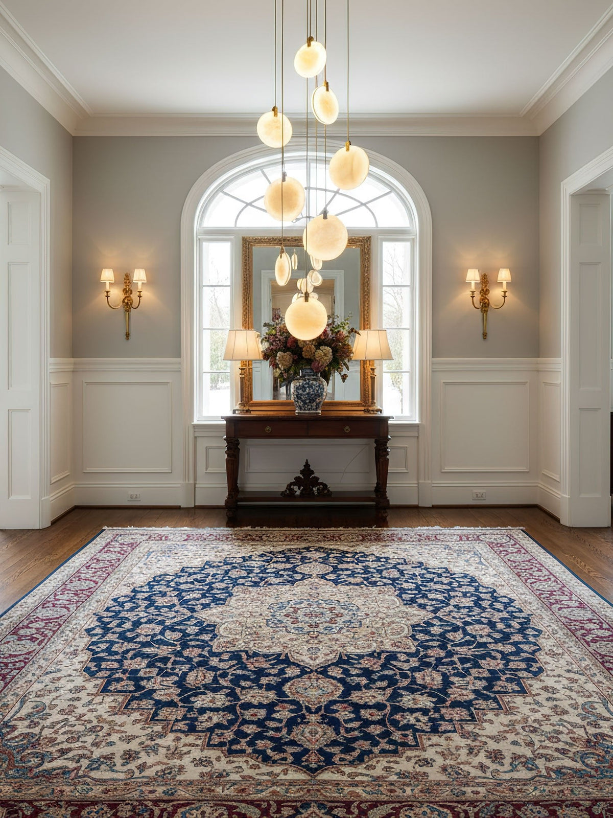 Alabaster disc pendants of this Clérachic cluster hang over a hallway with an arched window, a console table and a blue patterned rug.