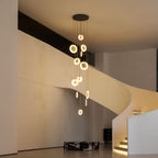 A Clérachic alabaster disc cluster glows warm gold in a white curved-stair hall, with a black ceiling plate and lit steps.