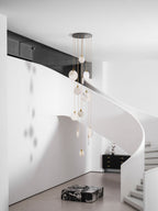 Clérachic alabaster discs unlit in a daylit white stair hall, hanging beside a black sideboard and a marble block.