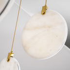 Close view of a pale, softly veined alabaster disc and gold hanger on this Clérachic pendant, with a brass rod beside it.