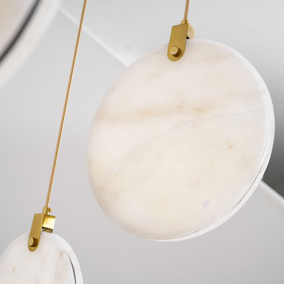 Close view of a pale, softly veined alabaster disc and gold hanger on this Clérachic pendant, with a brass rod beside it.
