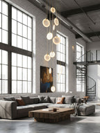 Clérachic alabaster disc pendants hang in a white-brick loft with tall black-framed windows, a grey corner sofa and a spiral stair.