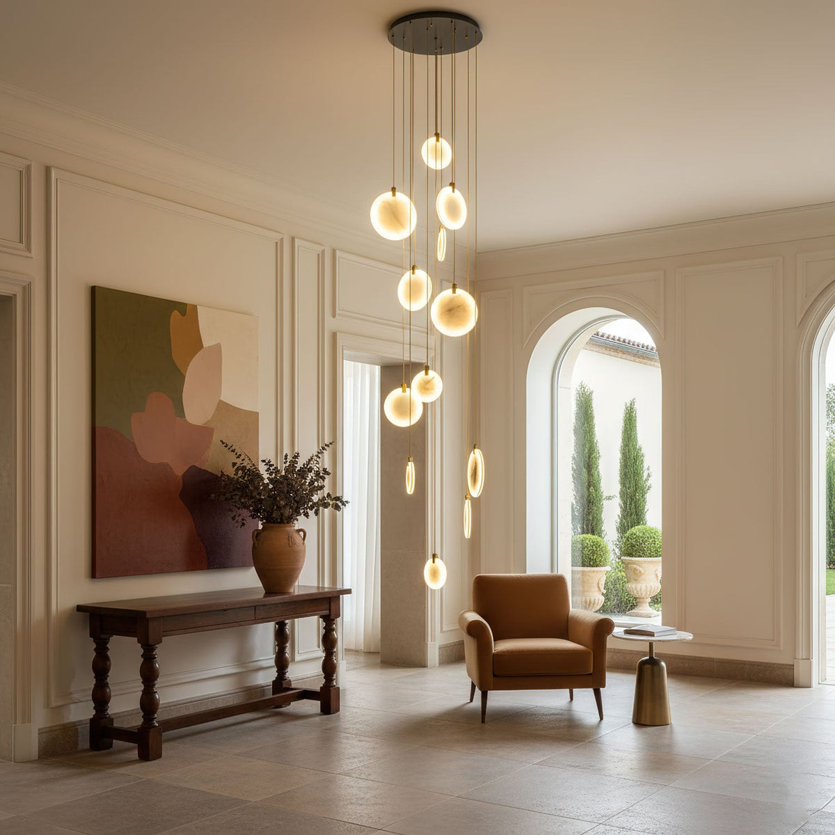 A Clérachic cluster of lit alabaster discs on a black ceiling plate in a cream hall, with a carved console and a rust armchair.