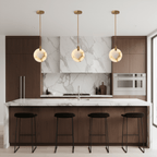 Three Clérachic alabaster disc pendants hang in a row over a marble and walnut kitchen island with four black stools.