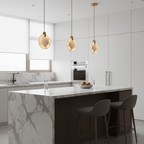 Three alabaster disc pendants from Clérachic in a white kitchen, over a marble island with dark grey stools and a bowl of fruit.
