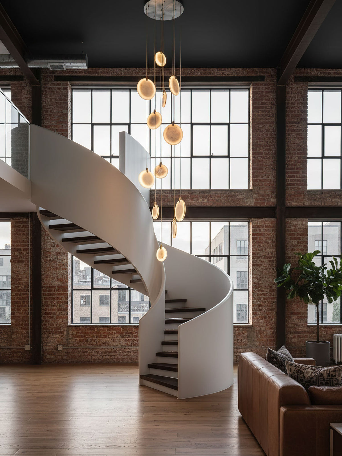 Alabaster disc pendants from Clérachic hang in a brick loft with high steel windows and a white spiral staircase.