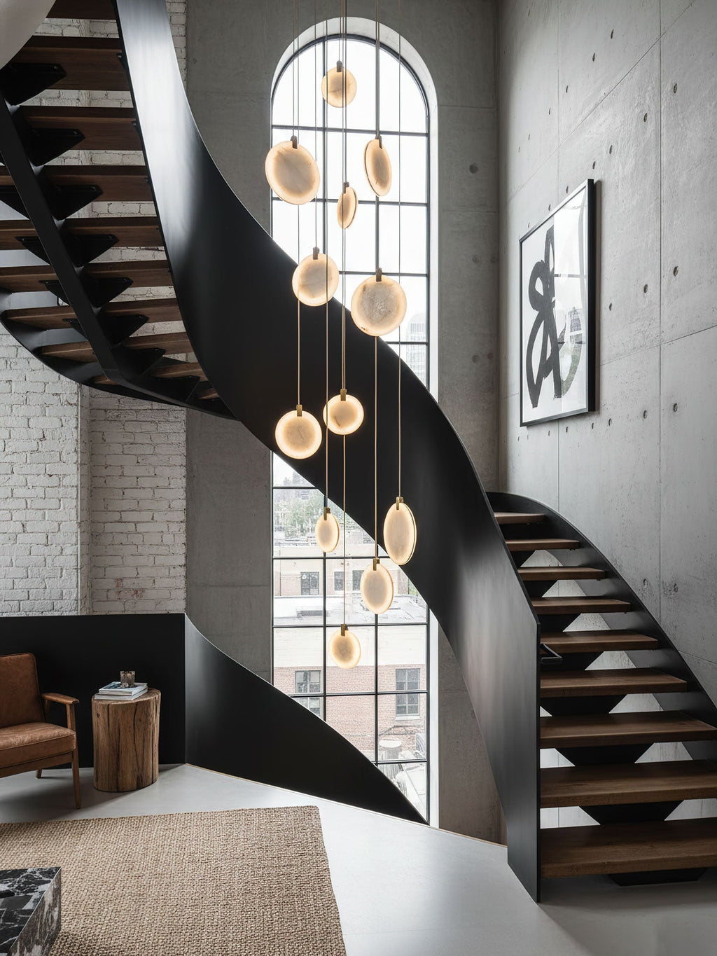 Lit alabaster discs of this Clérachic pendant hang past a black spiral staircase with timber treads, beside a tall arched window.