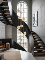 Lit alabaster discs of this Clérachic pendant hang past a black spiral staircase with timber treads, beside a tall arched window.