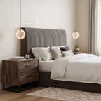 Two Clérachic alabaster disc pendants hang at either side of a bed with a grey headboard, above a rustic wood bedside chest.