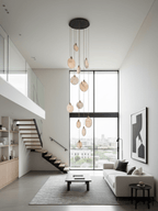 A Clérachic alabaster disc cluster on a dark ceiling plate hangs in front of a tall window in a minimal living room with an open staircase.