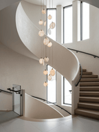 Alabaster disc pendants from Clérachic hang beside a curving pale staircase with timber steps and tall narrow windows.