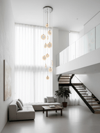 Clérachic alabaster disc pendants hang in front of sheer floor-length curtains in a white room with a mezzanine and a pale sofa.