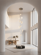A narrow Clérachic cluster of alabaster discs seen through an arched opening, above a plain rug and a sculptural wooden console.