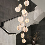 Close view of lit, veined alabaster discs from this Clérachic pendant, hanging beside a grey stone staircase wall and a dark vase.