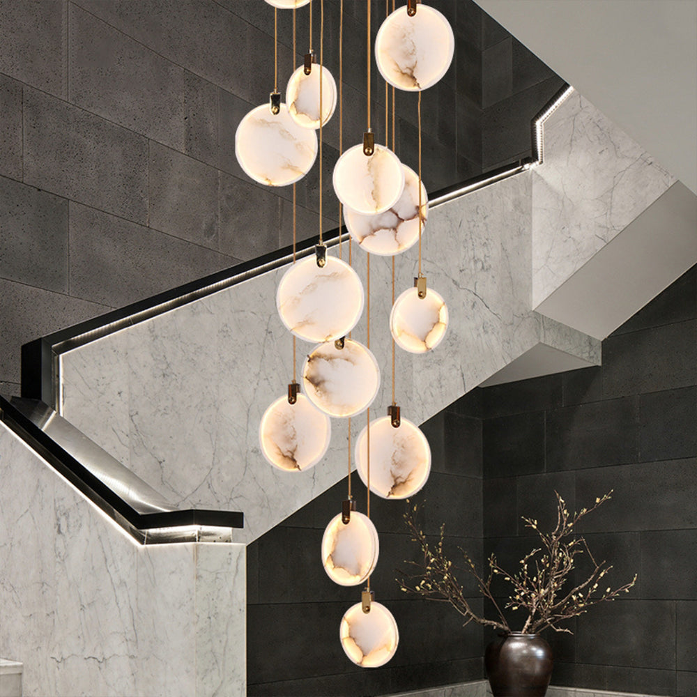 Close view of lit, veined alabaster discs from this Clérachic pendant, hanging beside a grey stone staircase wall and a dark vase.