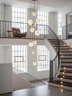 Alabaster disc pendants of this Clérachic cluster hang in a white-brick stairwell with black railings and steps lit from the side.