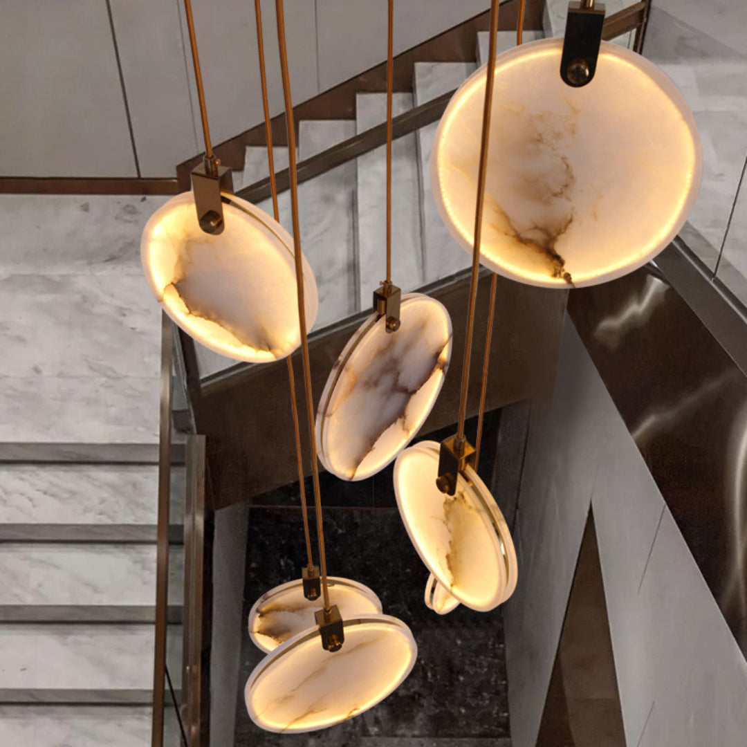 Looking down on lit alabaster discs of this Clérachic pendant, their veining showing, above a stone staircase with a glass balustrade.