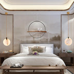 Two Clérachic alabaster disc pendants hang either side of a bed in a bedroom with a misty mountain mural and a round black wall frame.