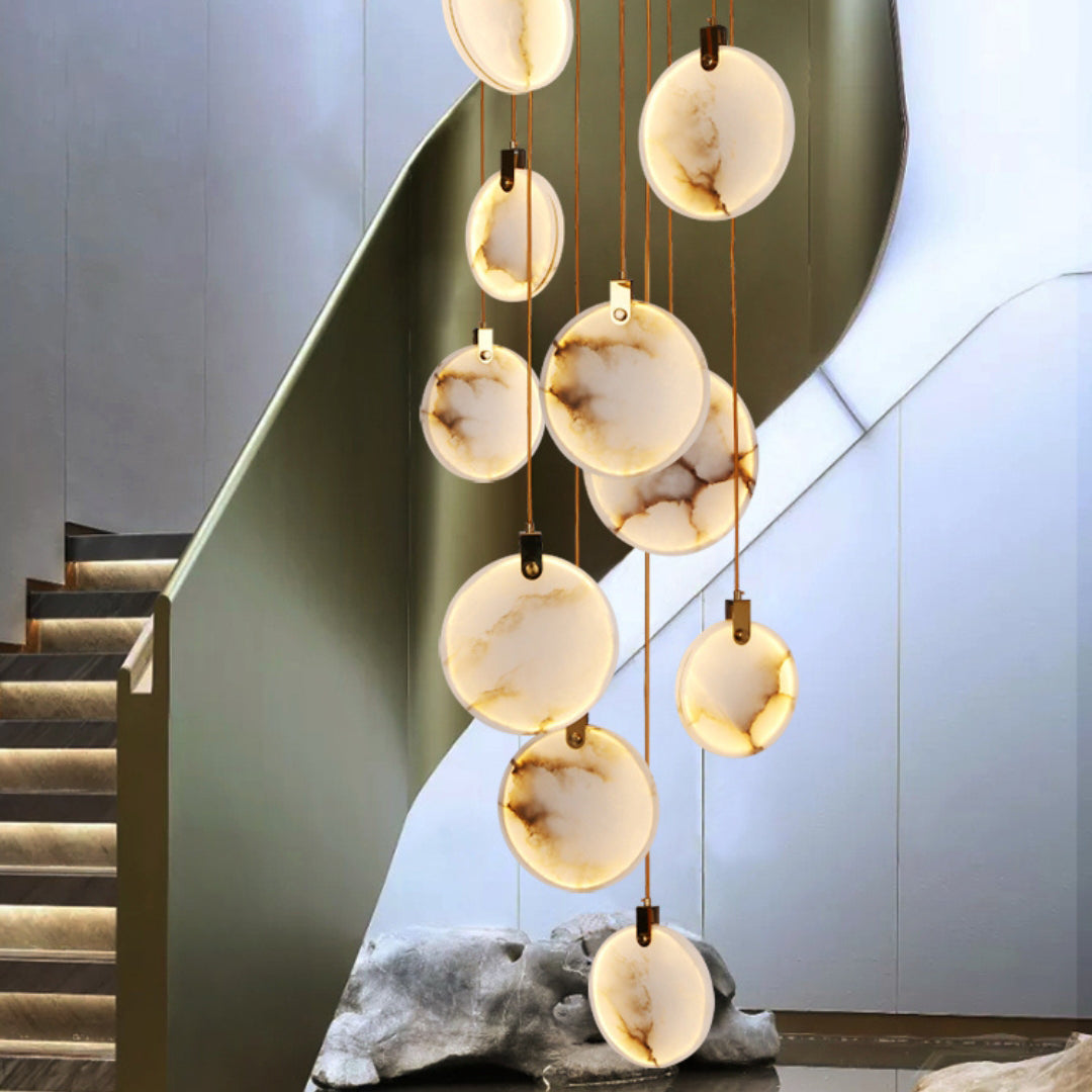 Clérachic alabaster discs hang at staggered heights beside a curving staircase with an olive-green rail and softly lit steps.