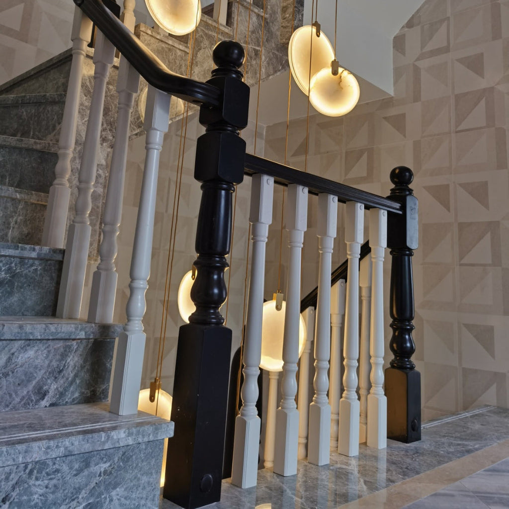 Clérachic alabaster discs hang above a staircase with white and black turned balusters and steps of grey stone.