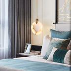 A single Clérachic alabaster disc pendant glows above a bed with teal and cream cushions, beside a framed photo on the bedside table.