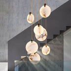Clérachic alabaster discs hang at different heights in front of a grey concrete wall and a dark staircase with glass panels.