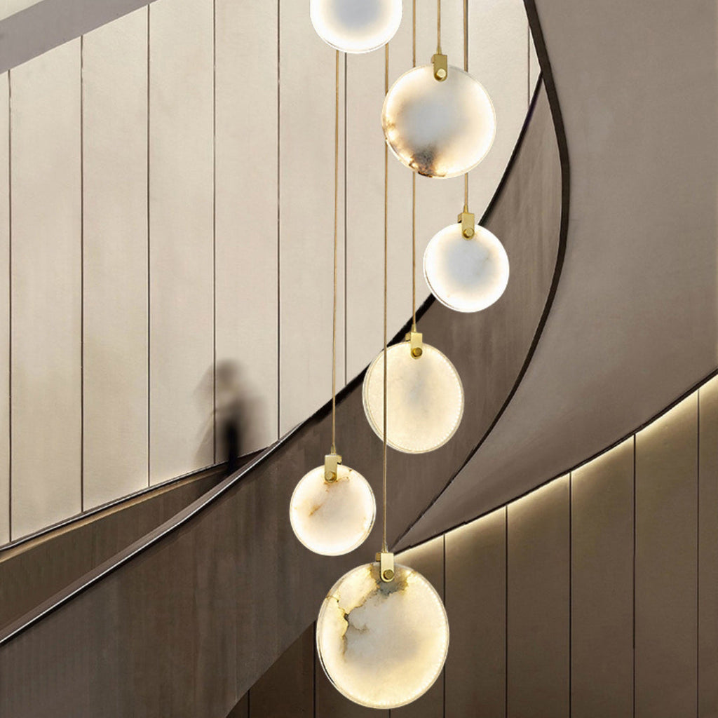 A column of Clérachic alabaster disc pendants with brass fittings hangs beside a curved wall, with a blurred figure on the stairs.