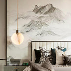 One Clérachic alabaster disc pendant on a tan cord hangs before a mountain landscape mural, above a bed with patterned cushions.