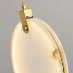 Close view of the brass hanger and the veined alabaster edge of one lit disc on this Clérachic pendant, on a grey backdrop.